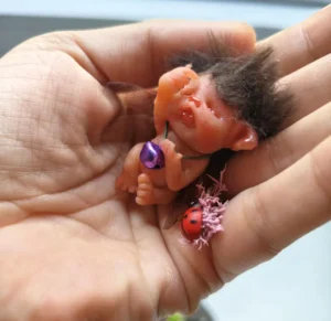 Por encargo 6 Escultura miniatura de un hada bebé de arcilla polimérica descansando sobre la palma de una mano junto a una mariquita.